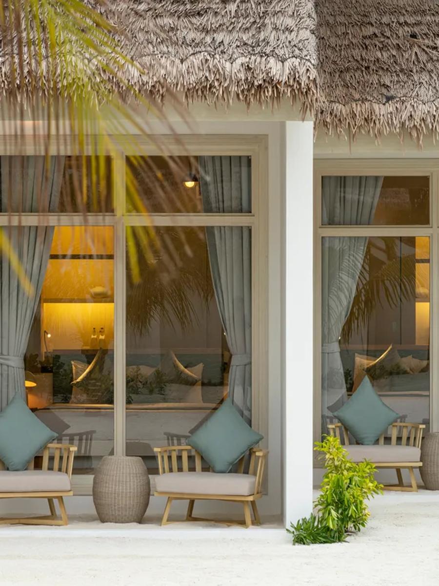 The thatched-roof entrance of a Beach Villa at Bandos, with lounge chairs set on a sandy porch behind a palm frond