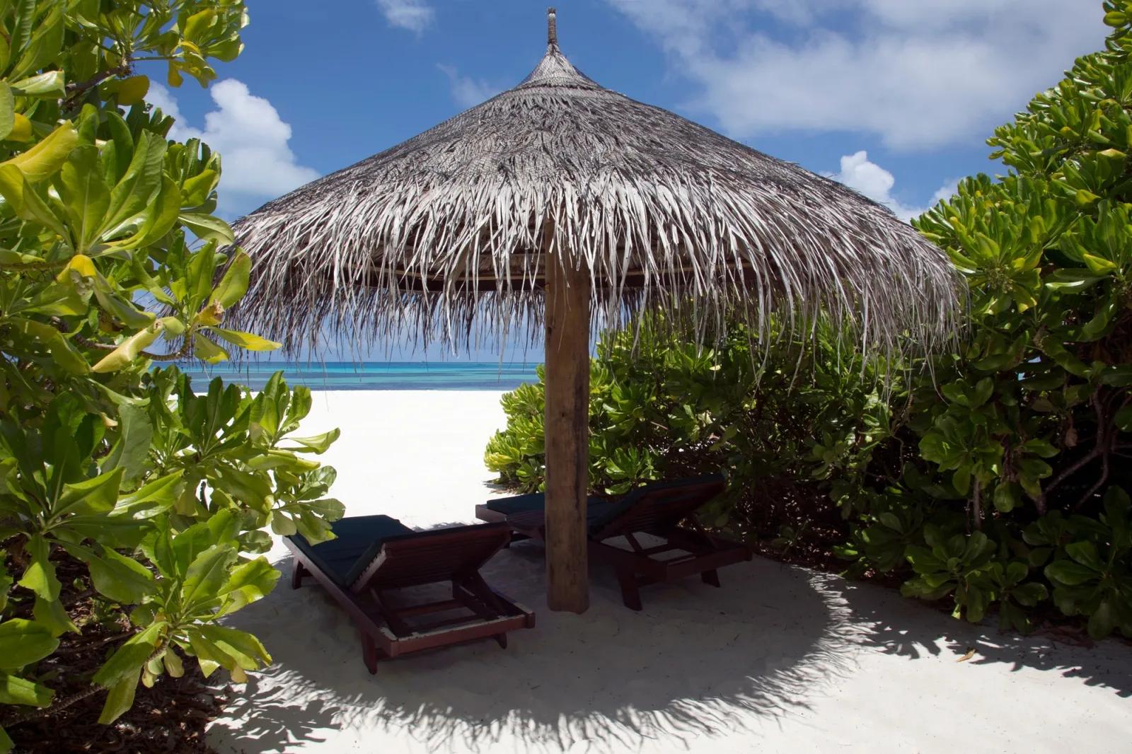 A thatched sunshade with wooden loungers on white sand, turquoise water beyond