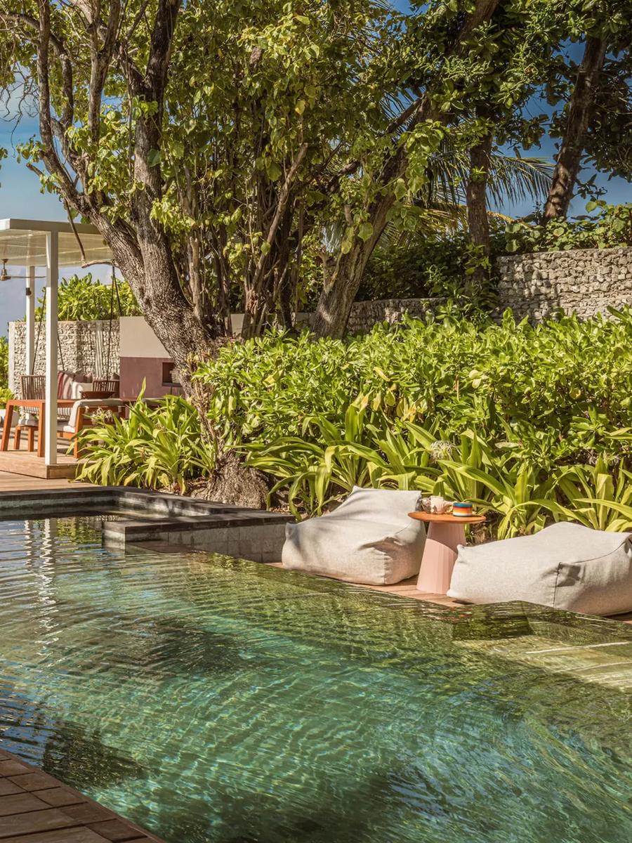 A Family Oceanfront Bungalow's pool deck beneath palm trees, with a shaded dining pavilion and beach visible through the foliage