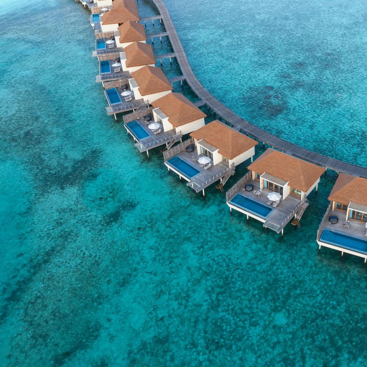 Radisson Blu Resort Maldives' curved row of overwater villas seen directly from above, private pools and a wooden jetty tracing the reef edge