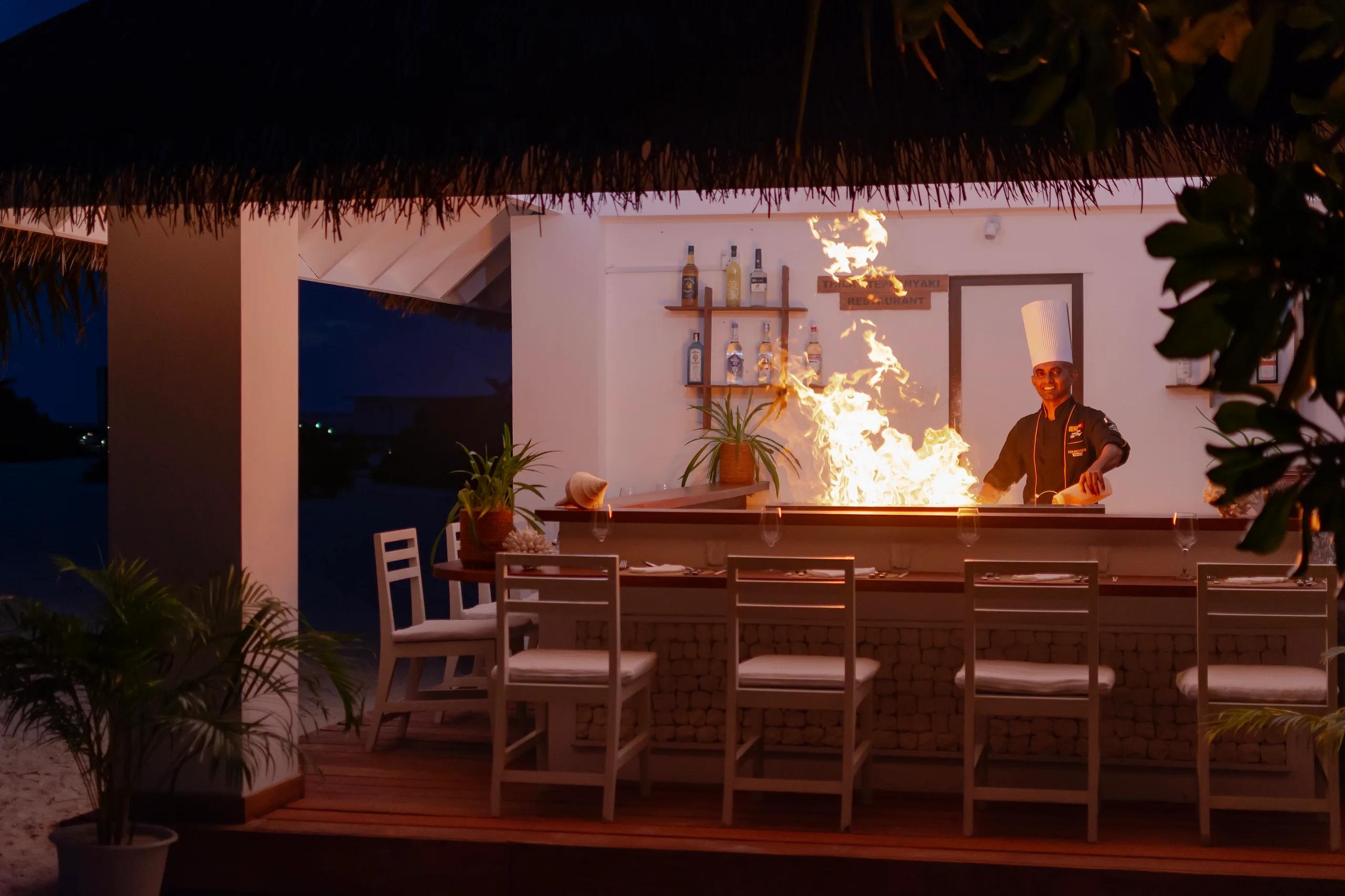 A chef performing teppanyaki live-cooking with a flame at Thila Japanese Restaurant, Diamonds Athuruga