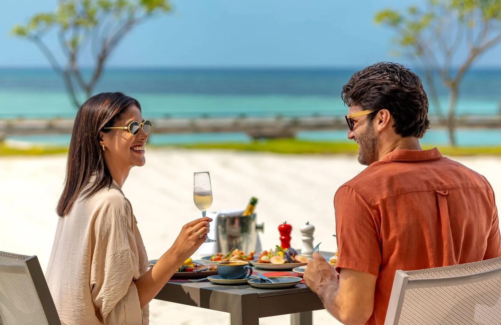 A couple sharing a meal at THE PALMS, the resort's all-day restaurant, with the lagoon behind them