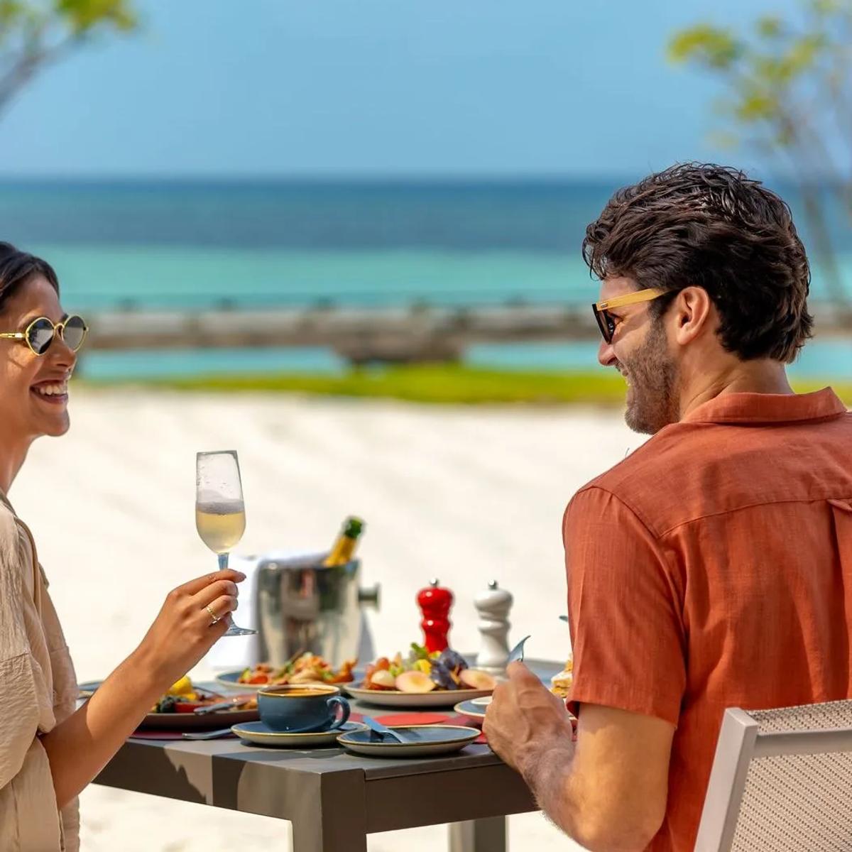 A couple sharing a meal at THE PALMS, the resort's all-day restaurant, with the lagoon behind them
