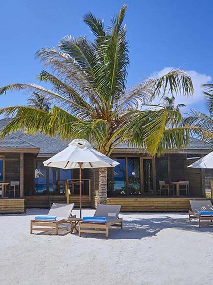 The exterior of a Dheru Island Three Bedroom Villa, three loungers and umbrellas set along its beachfront deck
