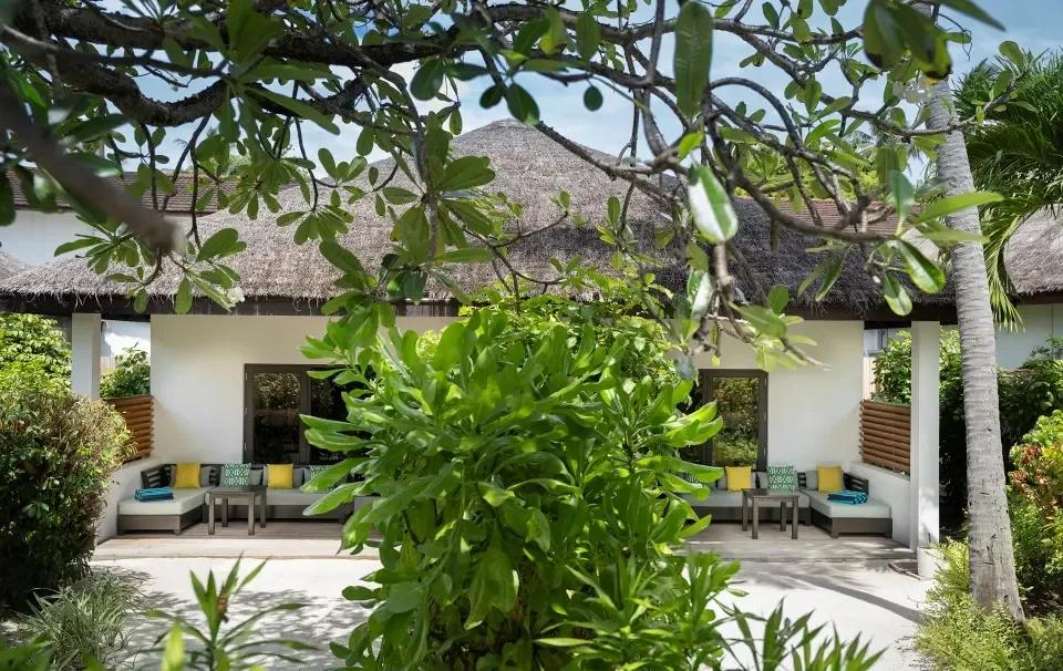 The Two Bedroom Deluxe Villa's outdoor lounge area, seen through the branches of a frangipani tree