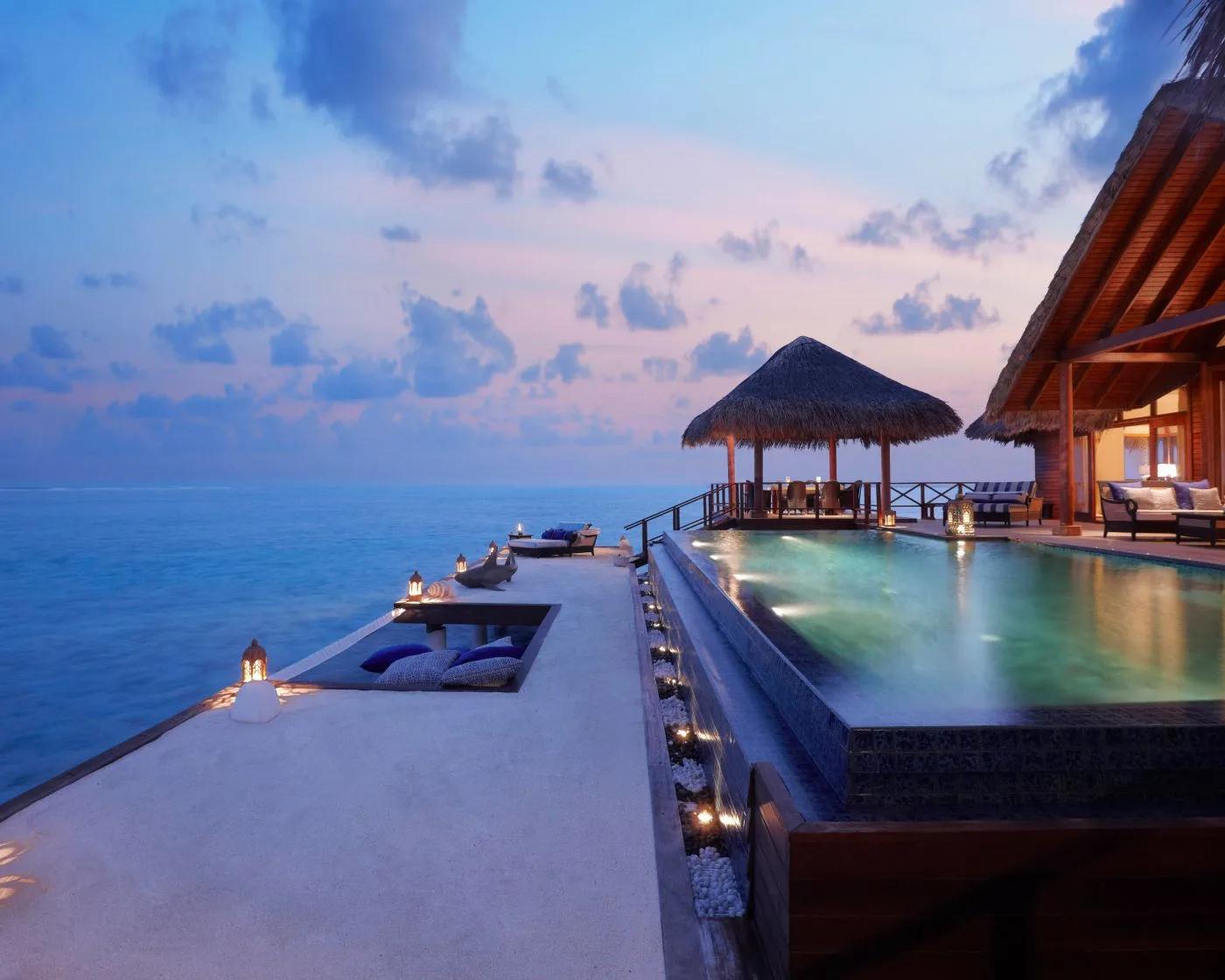 The Rehendhi Presidential Suite's private pool and overwater pavilion at dusk, lanterns lit along the deck