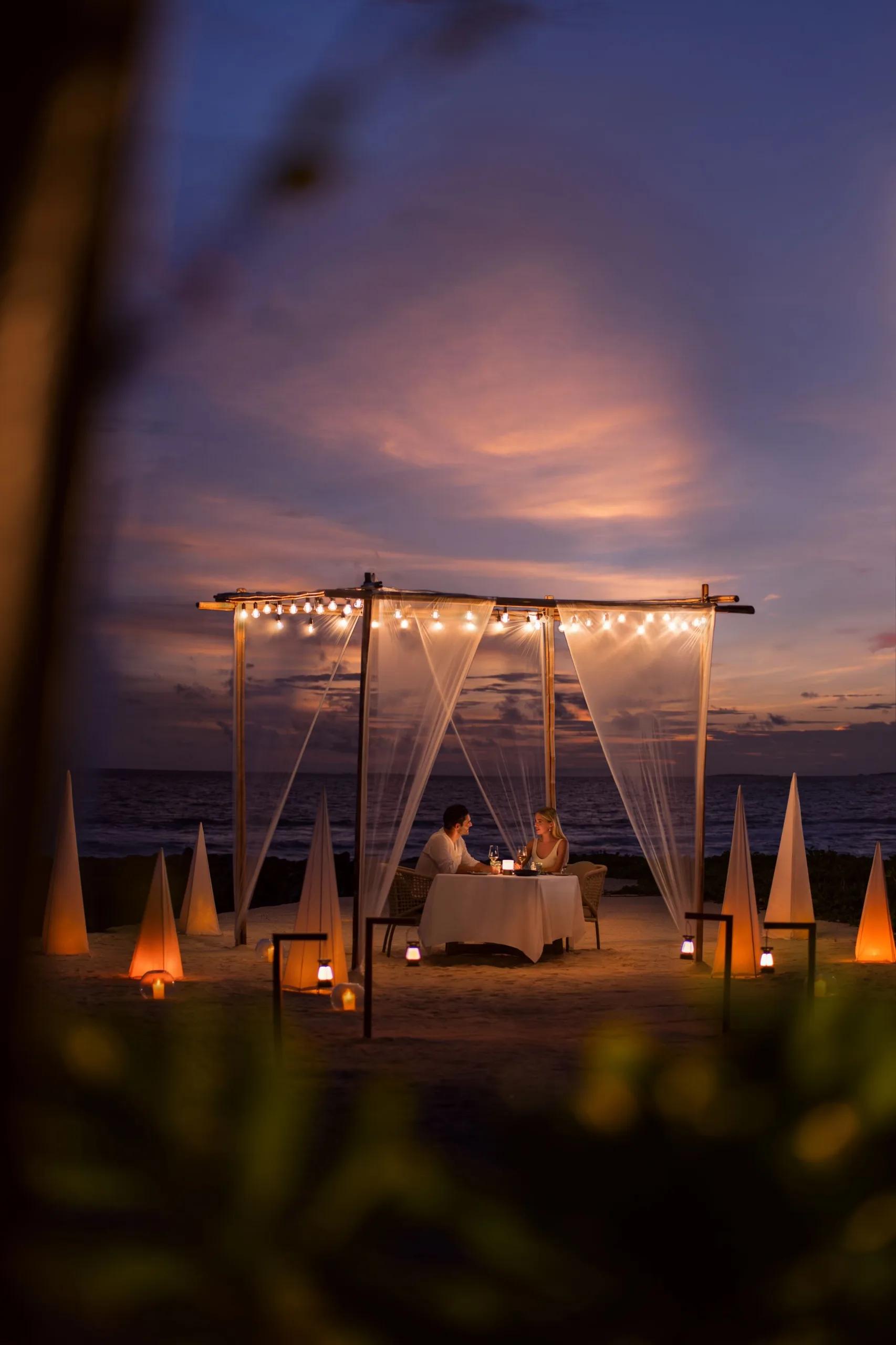 A private candlelit dinner set up on the beach at sunset, part of the resort's Celebrate Love by the Ocean programme