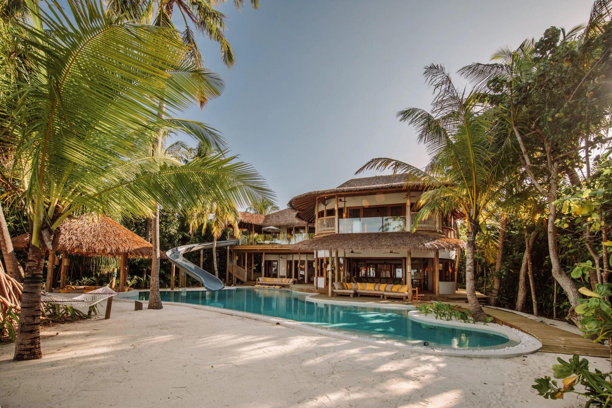 Villa 31, a 5-Bedroom Residence, seen from the garden side — multiple thatched pavilions around a long pool with a slide, palm trees framing the deck