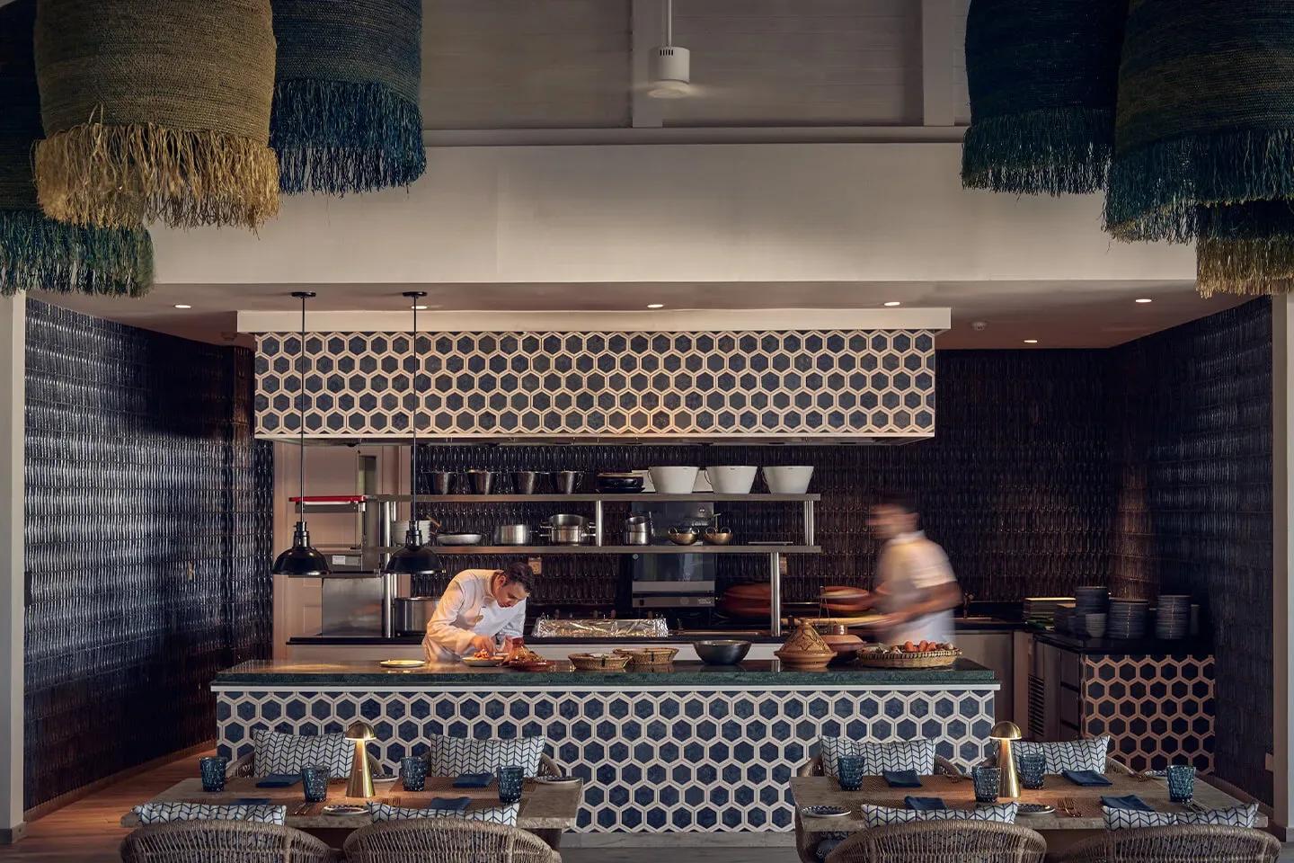 Arabian Grill's dark honeycomb-tiled open kitchen, with two chefs preparing dishes in view of patterned banquette seating