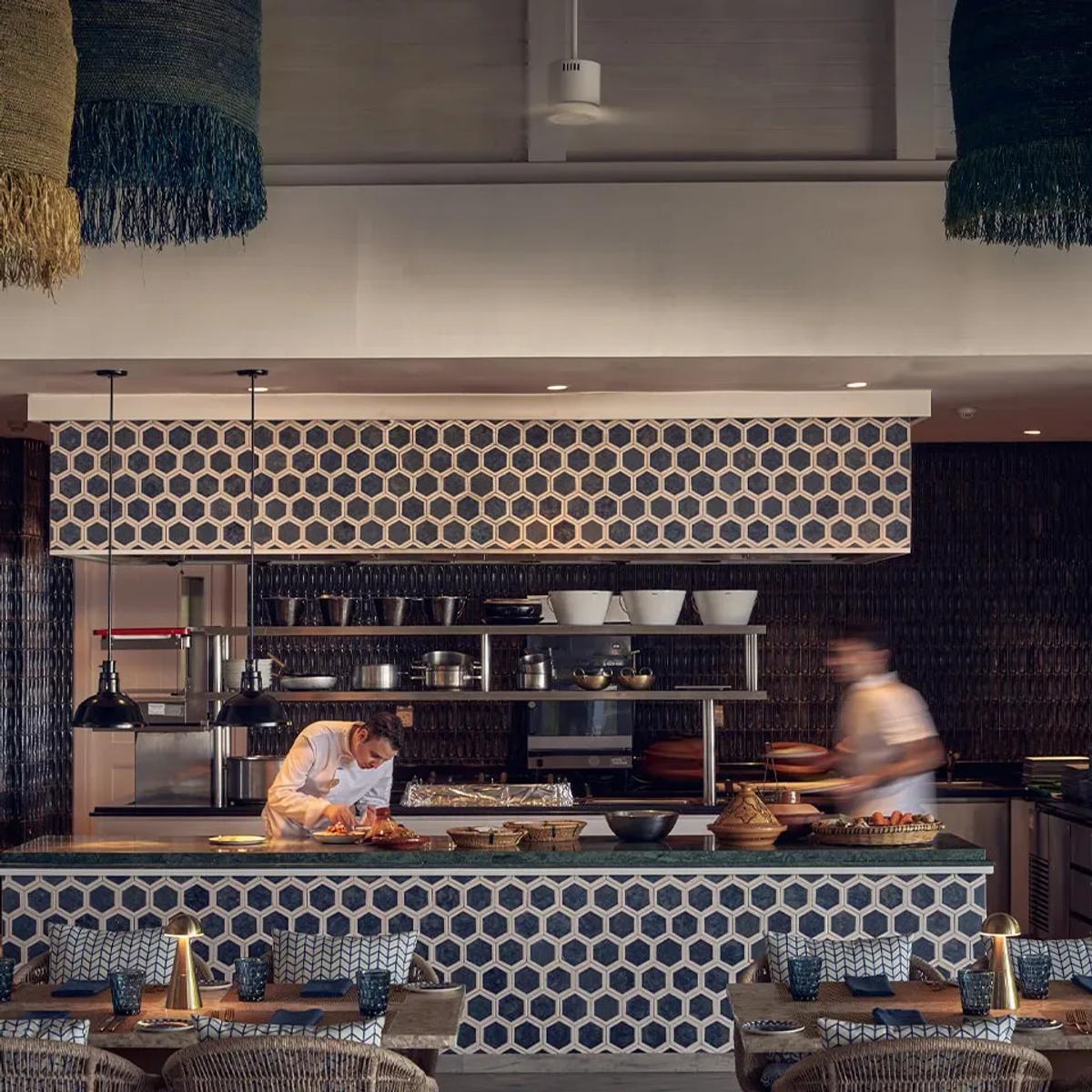Arabian Grill's dark honeycomb-tiled open kitchen, with two chefs preparing dishes in view of patterned banquette seating