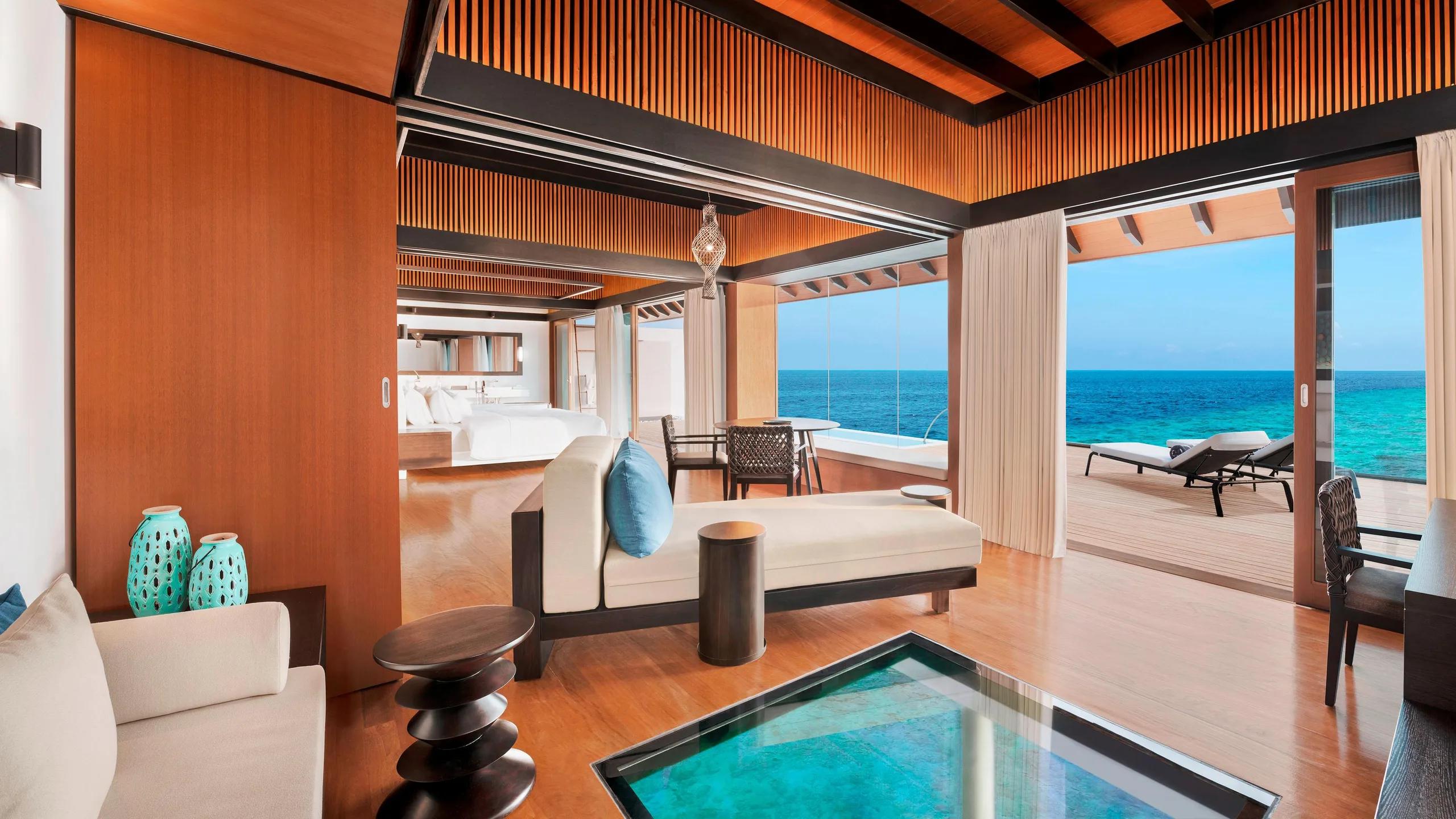 A glass floor panel set into a villa's living area, the reef visible below