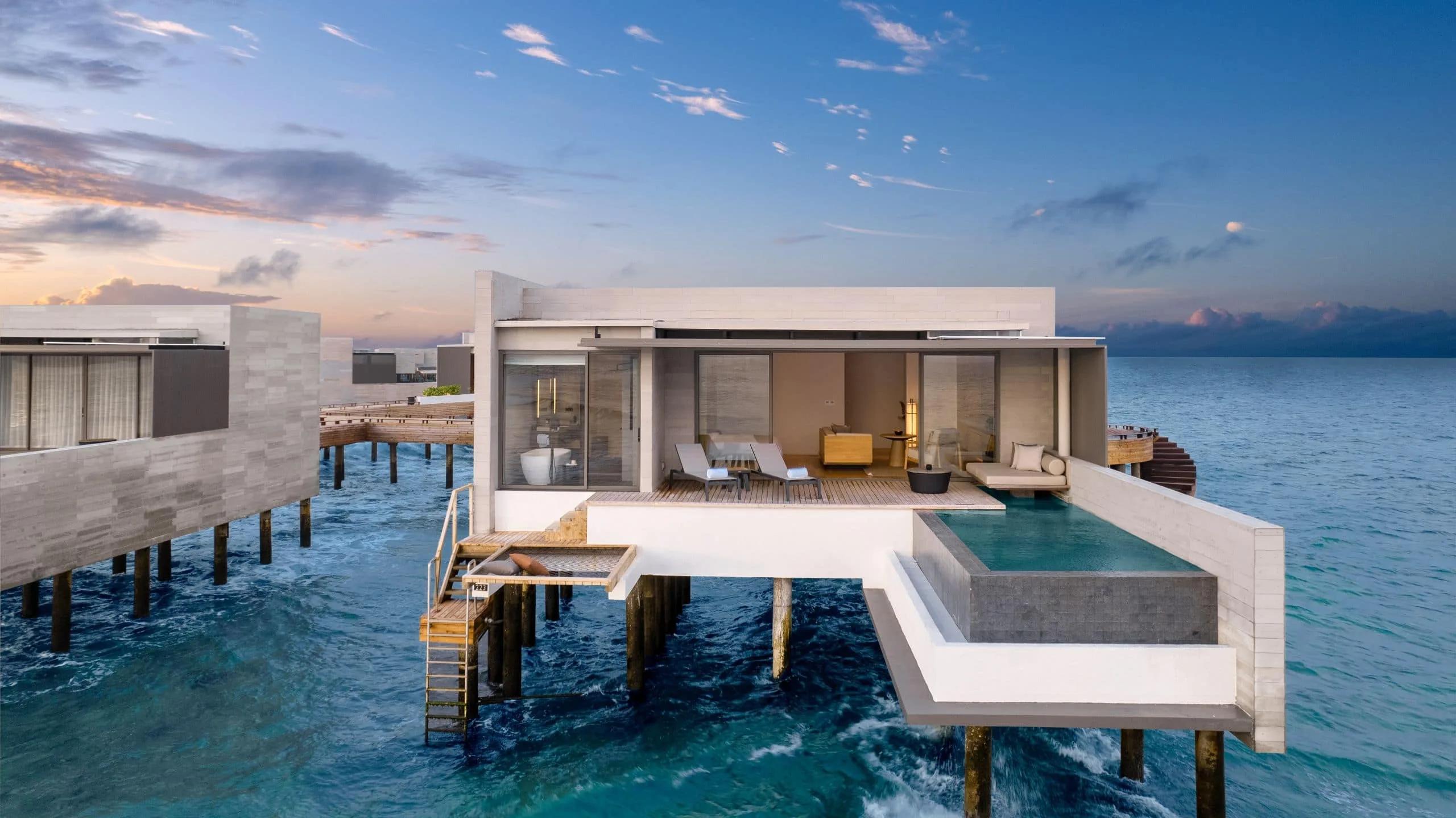 An overwater villa's exterior at dusk, lit against the darkening lagoon