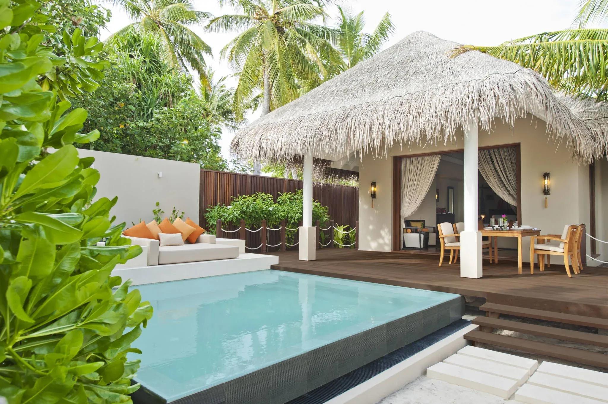 A Beach Villa's thatched pavilion, plunge pool, and shaded dining table set among palms