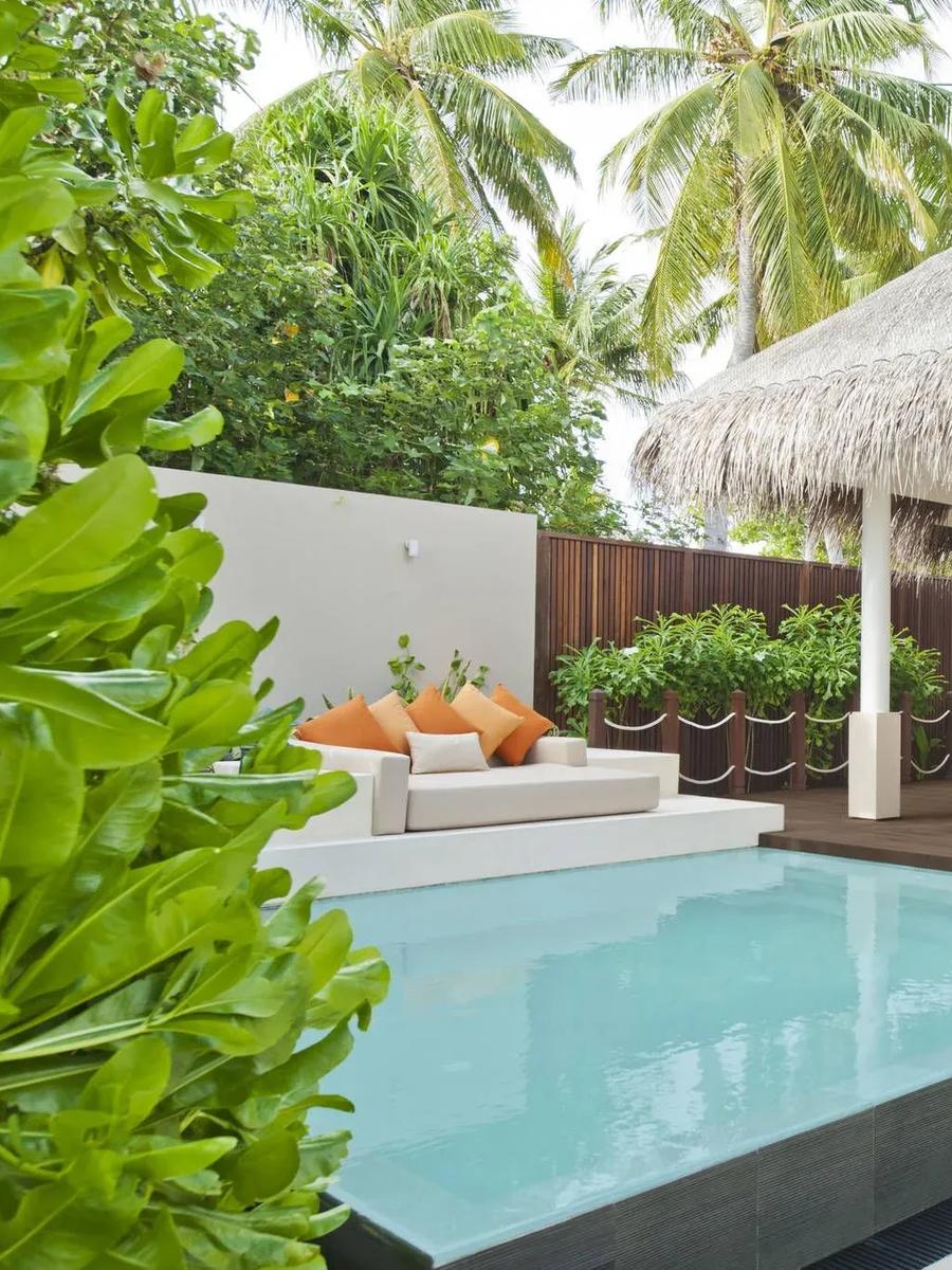 A Beach Villa's thatched pavilion, plunge pool, and shaded dining table set among palms