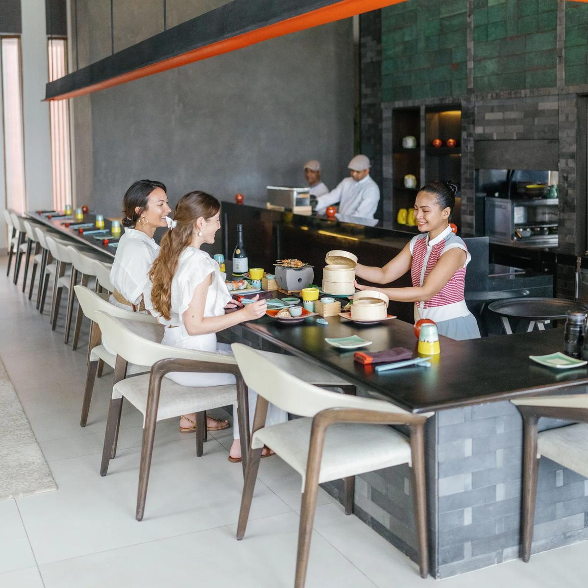 Chefs at The Diptyque's live-cooking counter serving bamboo steamers to a couple seated at the bar