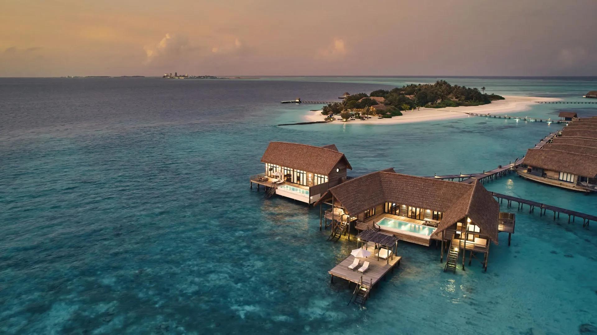 The Three-Bedroom COMO Sunset Villa's two joined wings, lit up over the lagoon at dusk