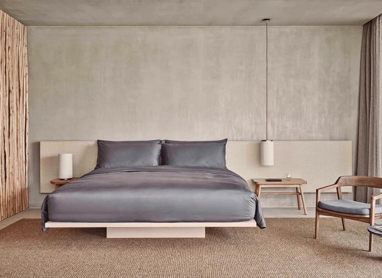 A pared-back bedroom at a Fari Studio, a floating timber platform bed set against a plain concrete wall
