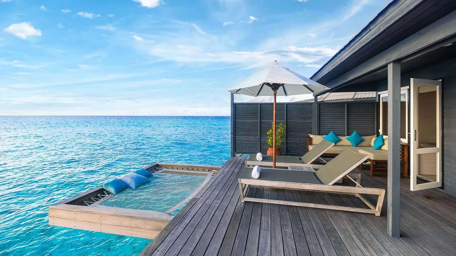 The deck of an Ocean Jacuzzi Water Villa, with a catamaran-net hammock suspended over the turquoise lagoon and a daybed sofa alongside