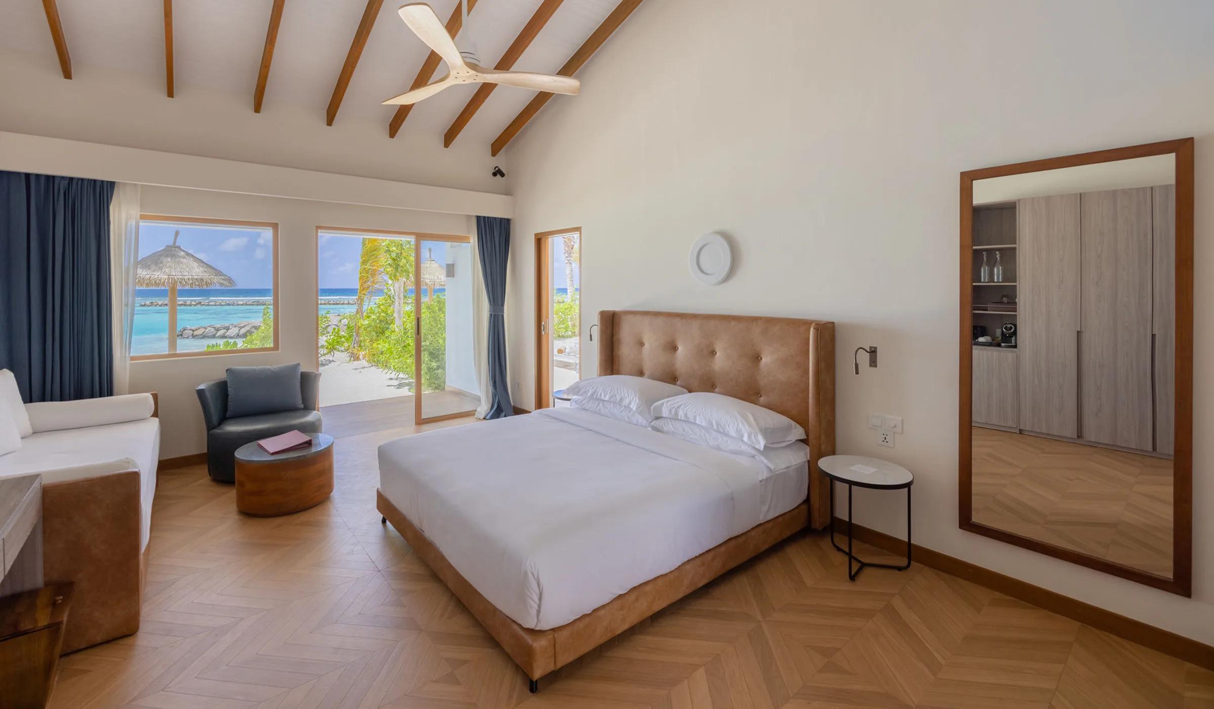A Family Beach Villa's bedroom, glass doors opening onto a garden path toward the beach umbrellas beyond
