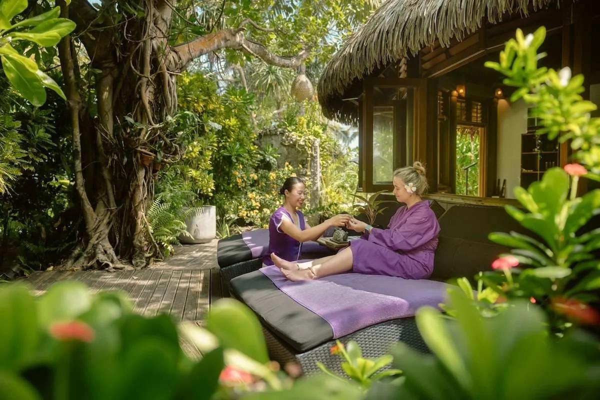 A guest receiving a treatment on Duniye Spa's open-air deck, shaded by a large tree and surrounded by tropical planting