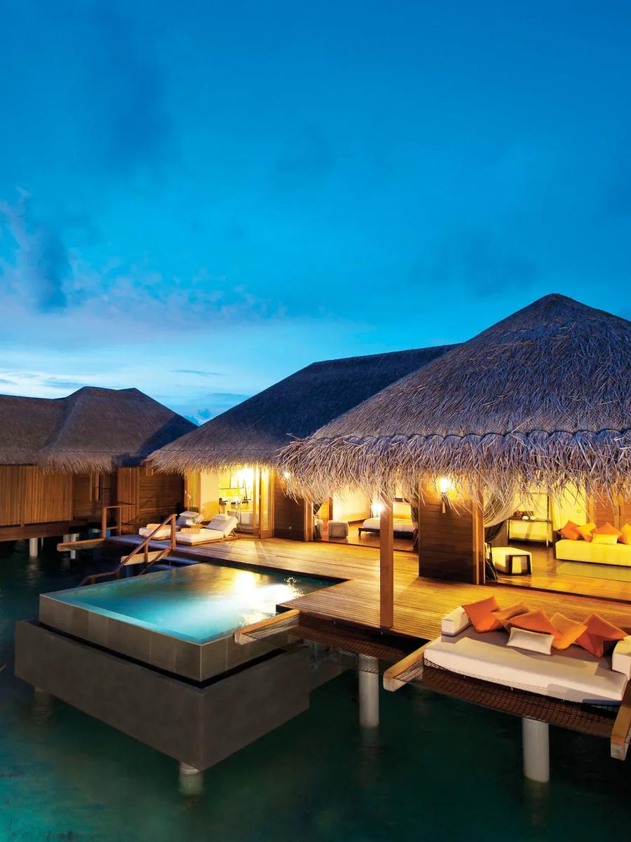 A row of Sunset Ocean Suites lit at dusk, overwater decks and plunge pools above the lagoon