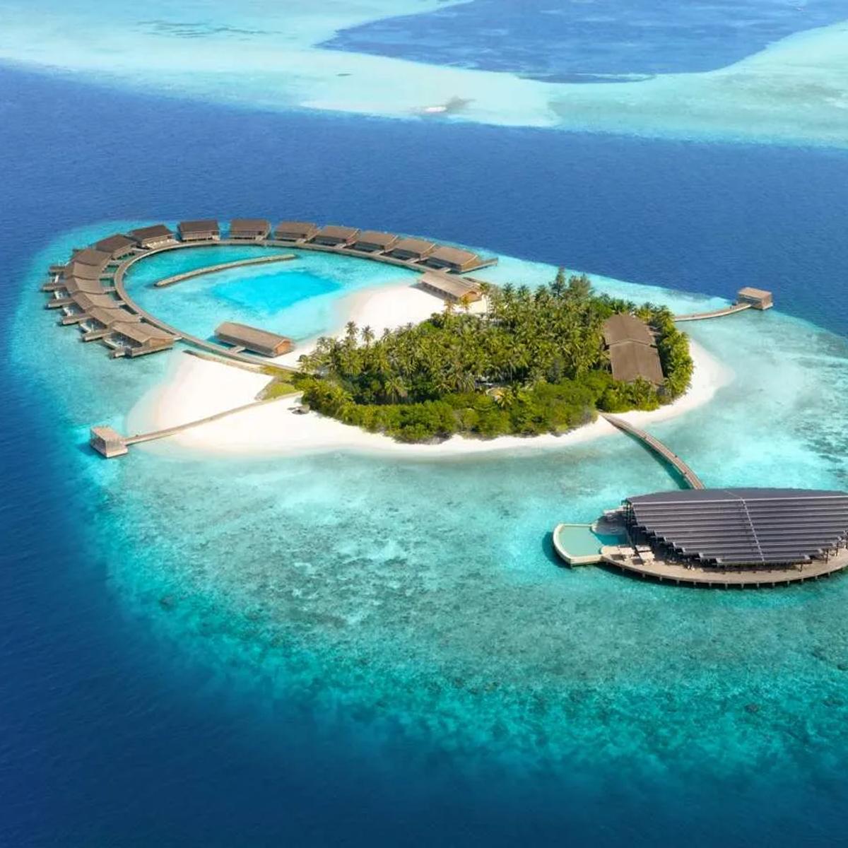 Kudadoo's private island seen from the air, its horseshoe of overwater residences and solar-roofed main building ringed by reef