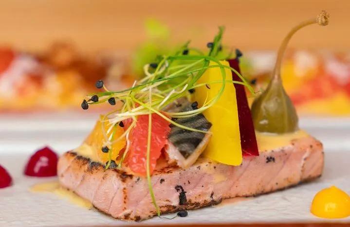 A small plate of seared fish with citrus, herbs and pickled vegetables, plated at LONU