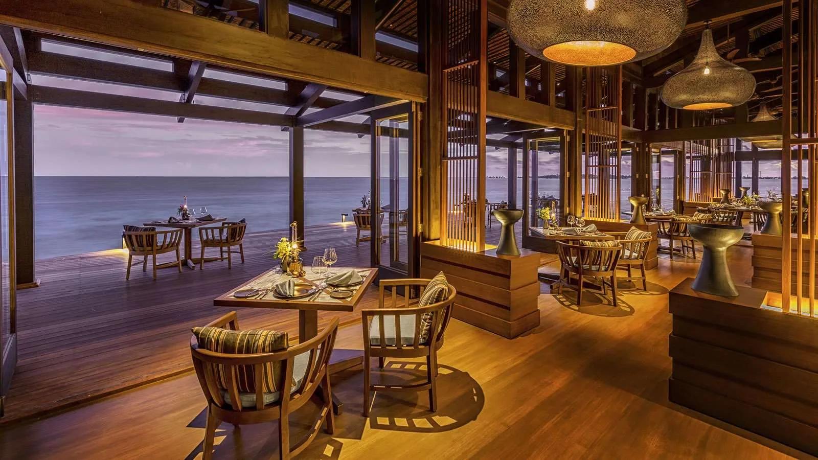The Retreat's air-conditioned dining room, open to the lagoon at dusk under woven pendant lights