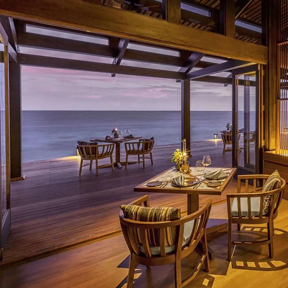 The Retreat's air-conditioned dining room, open to the lagoon at dusk under woven pendant lights