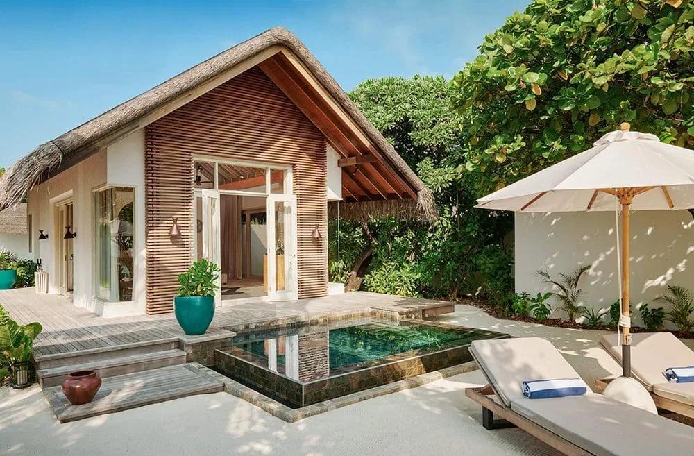 Exterior of a beachfront villa with a thatched roof and private plunge pool, palm trees framing the deck