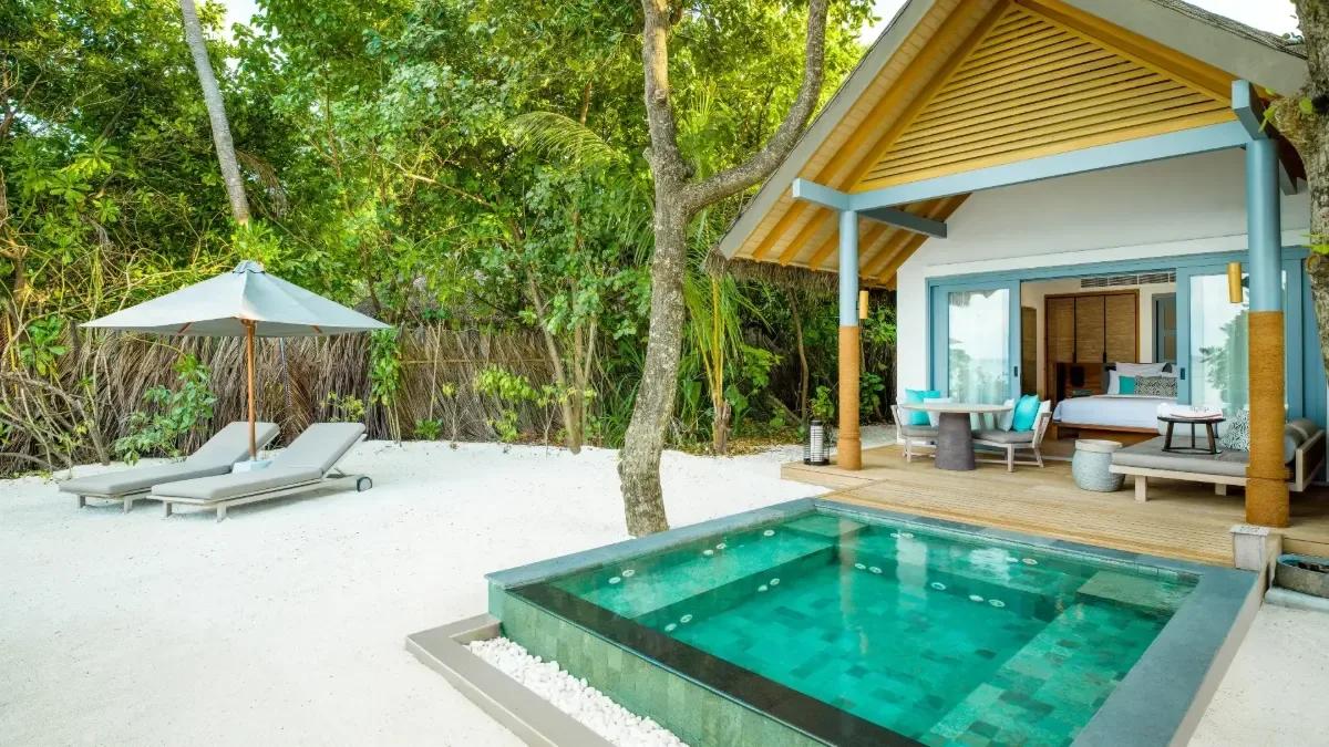Three connected thatched-roof pavilions of a Three Bedroom Beach Pool Residence, lit at dusk beside its pool