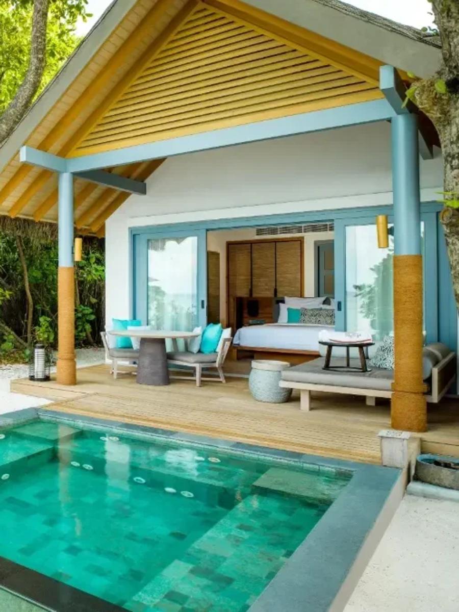 Three connected thatched-roof pavilions of a Three Bedroom Beach Pool Residence, lit at dusk beside its pool