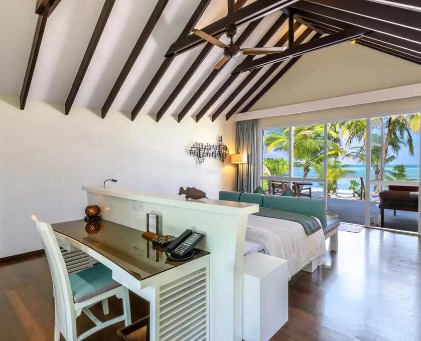 Deluxe Beach Villa interior with a dark-beamed ceiling, sofa, and sliding doors open to the beach