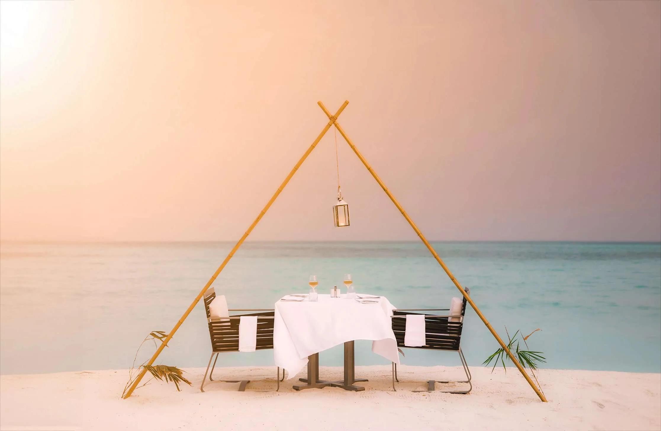 A private beach dinner table set beneath a bamboo frame at sunset, Hideaway Beach Resort & Spa