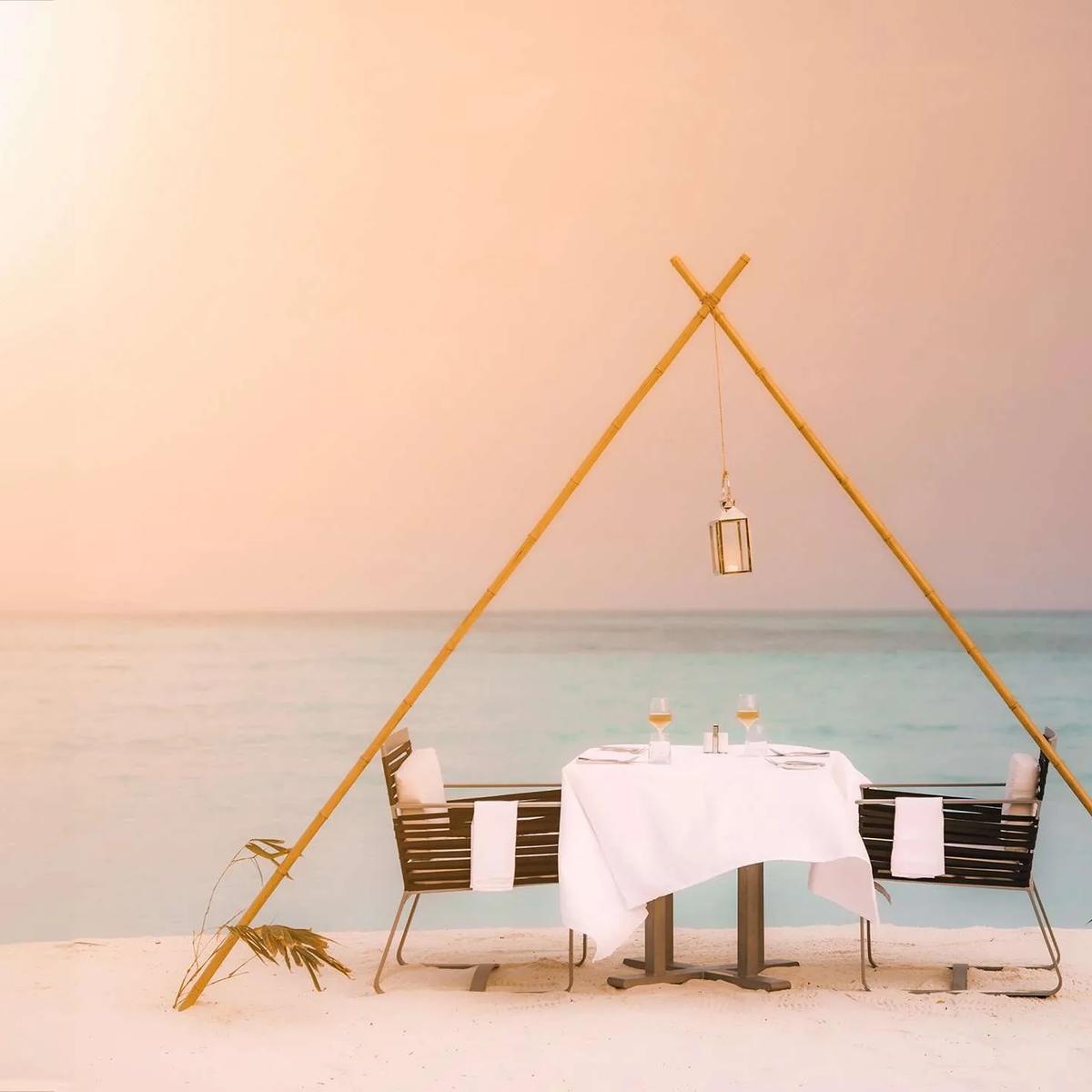 A private beach dinner table set beneath a bamboo frame at sunset, Hideaway Beach Resort & Spa