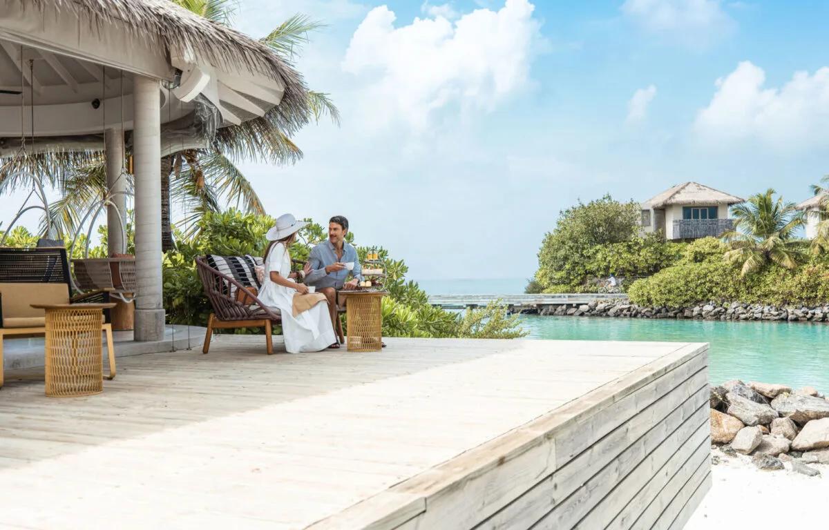 A couple taking afternoon tea from a tiered stand on The Retreat's overwater deck