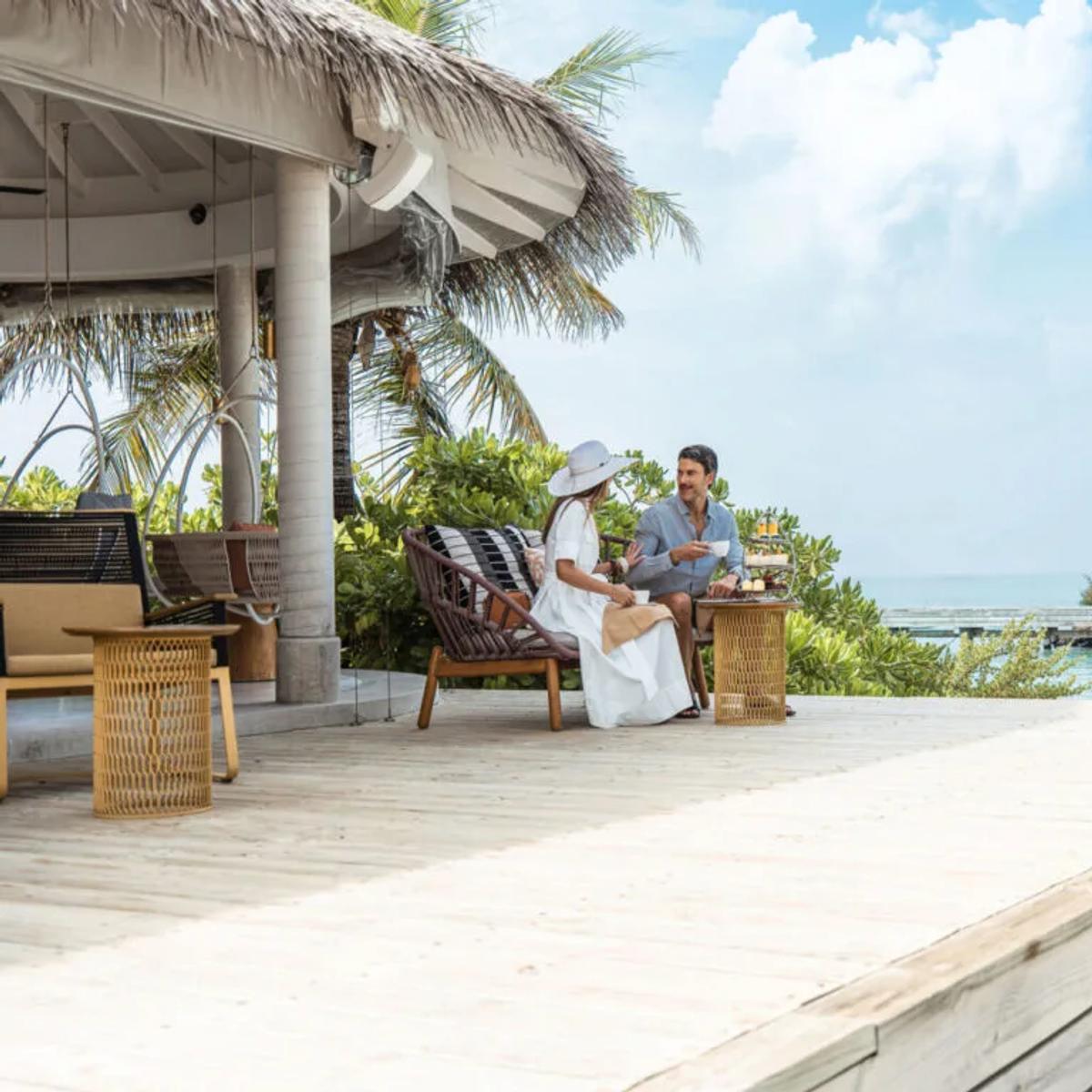 A couple taking afternoon tea from a tiered stand on The Retreat's overwater deck