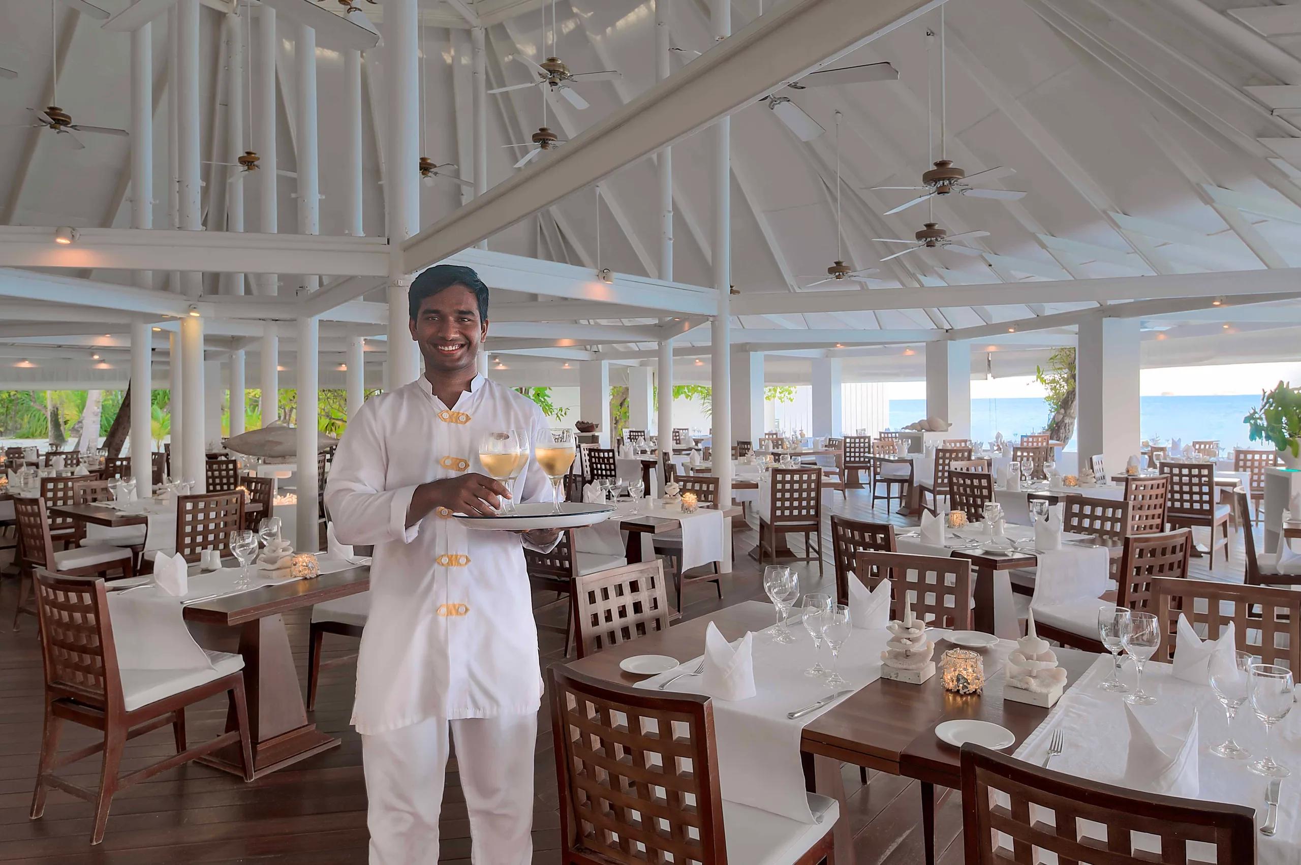 The high-raftered dining hall at Maakana Buffet Restaurant, with a waiter carrying drinks past rows of set tables