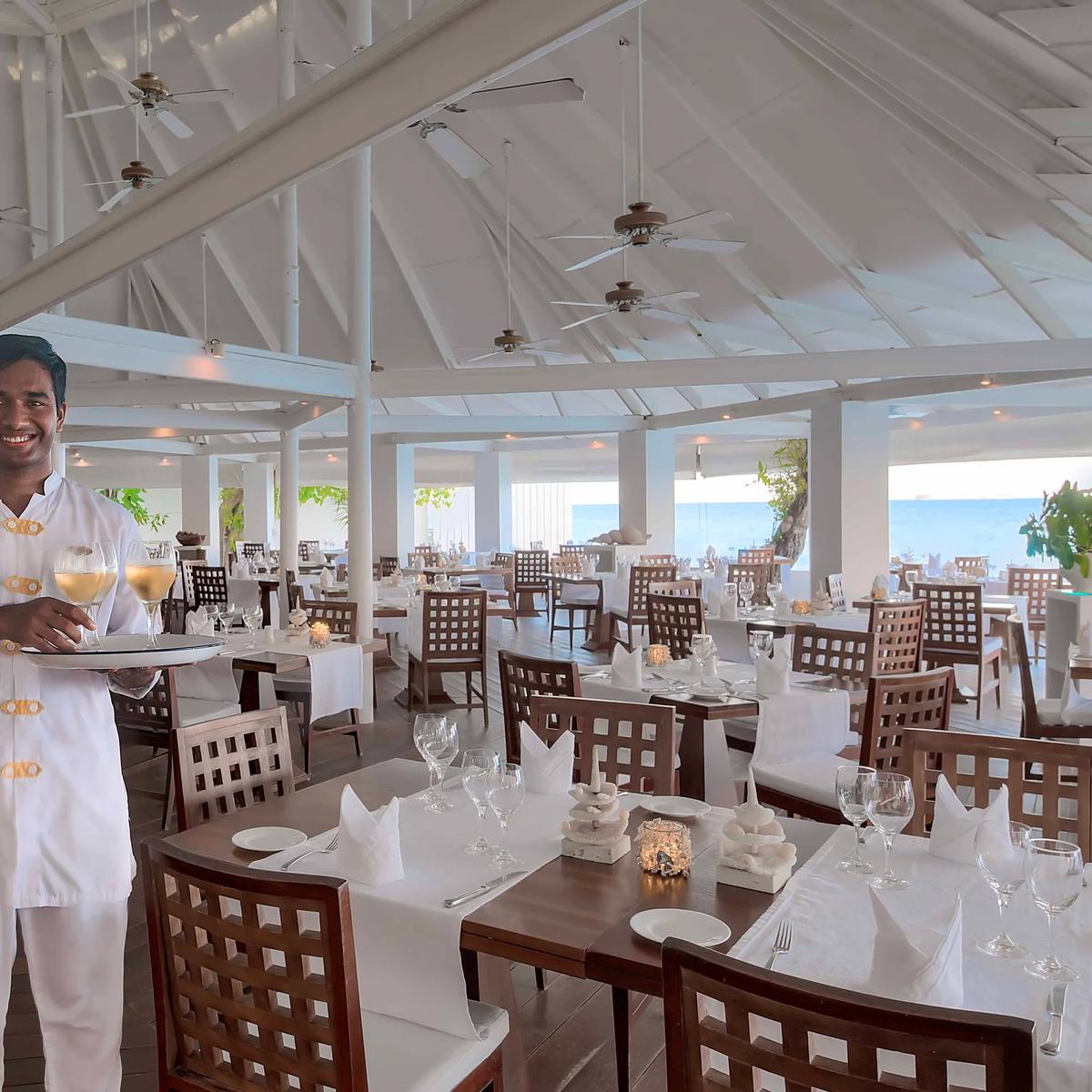 The high-raftered dining hall at Maakana Buffet Restaurant, with a waiter carrying drinks past rows of set tables