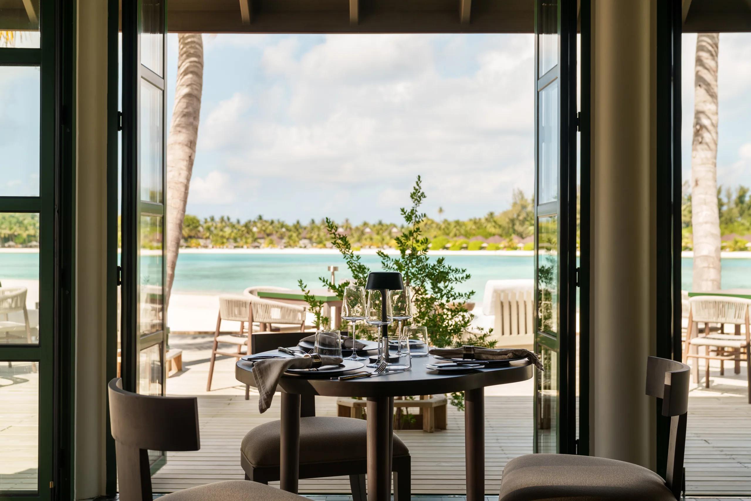A table set for two at Milano restaurant, open glass doors framing a view of the beach and lagoon at dusk