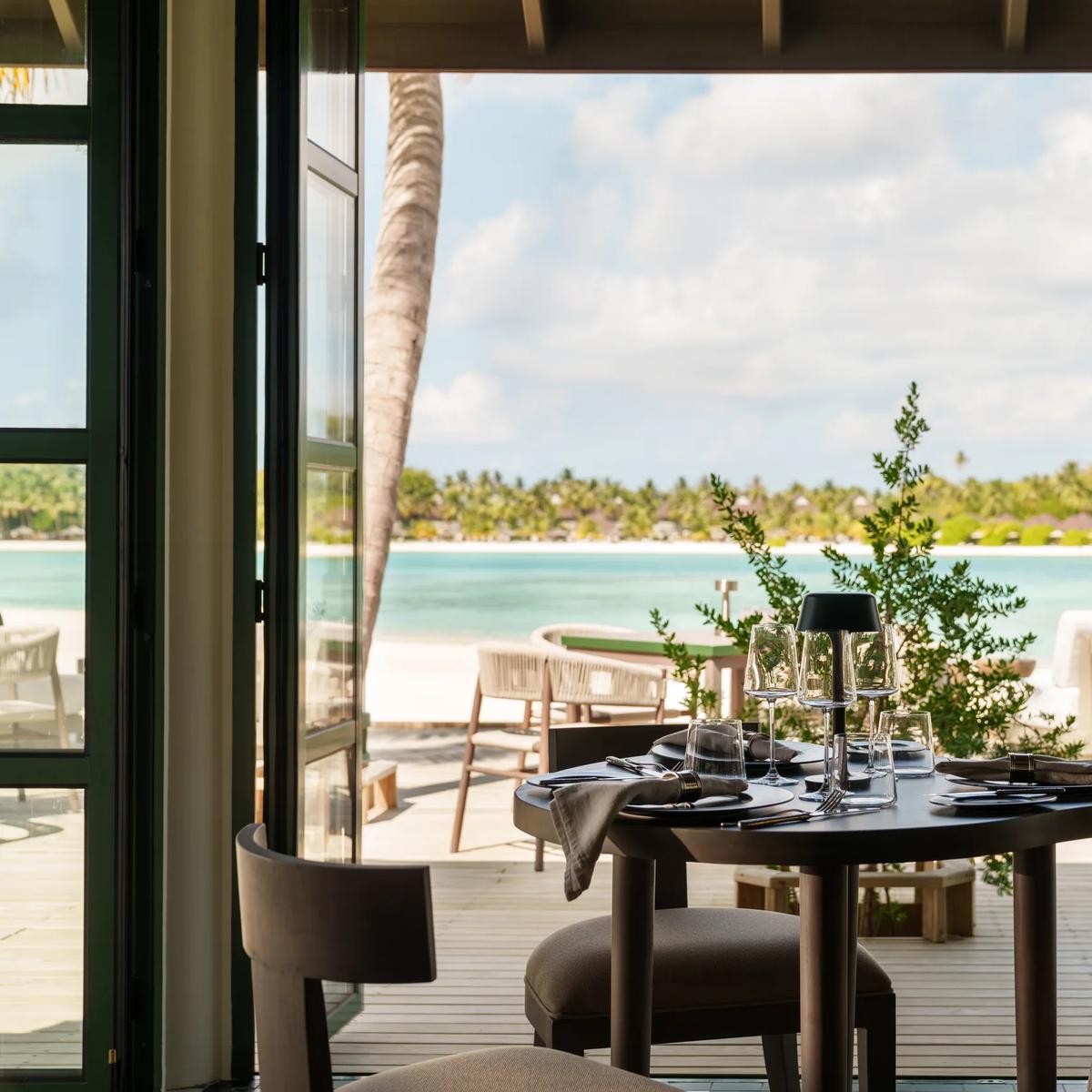 A table set for two at Milano restaurant, open glass doors framing a view of the beach and lagoon at dusk