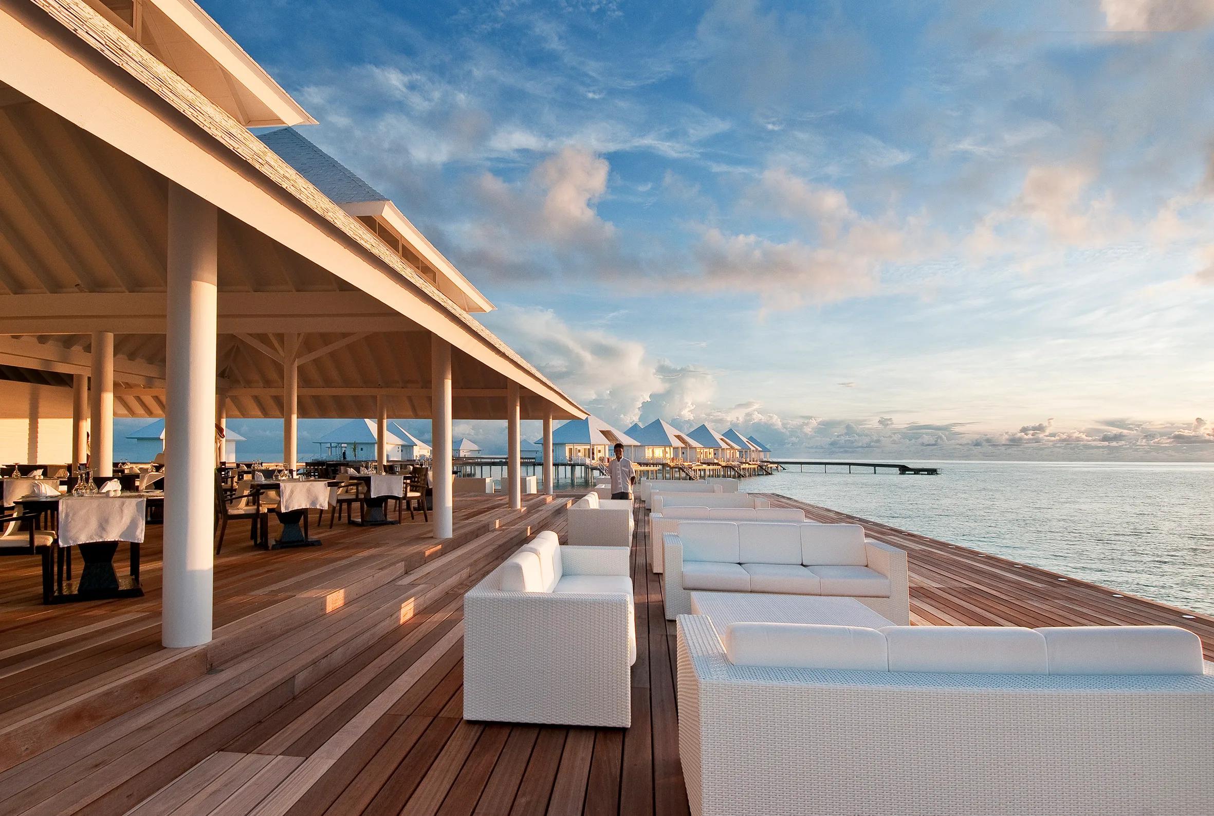 The overwater lounge deck near Aqua Over Water Bar at first light, white sofas set along the jetty rail