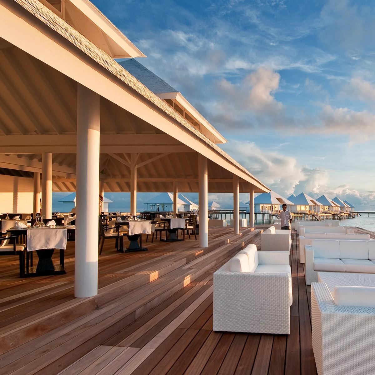 The overwater lounge deck near Aqua Over Water Bar at first light, white sofas set along the jetty rail