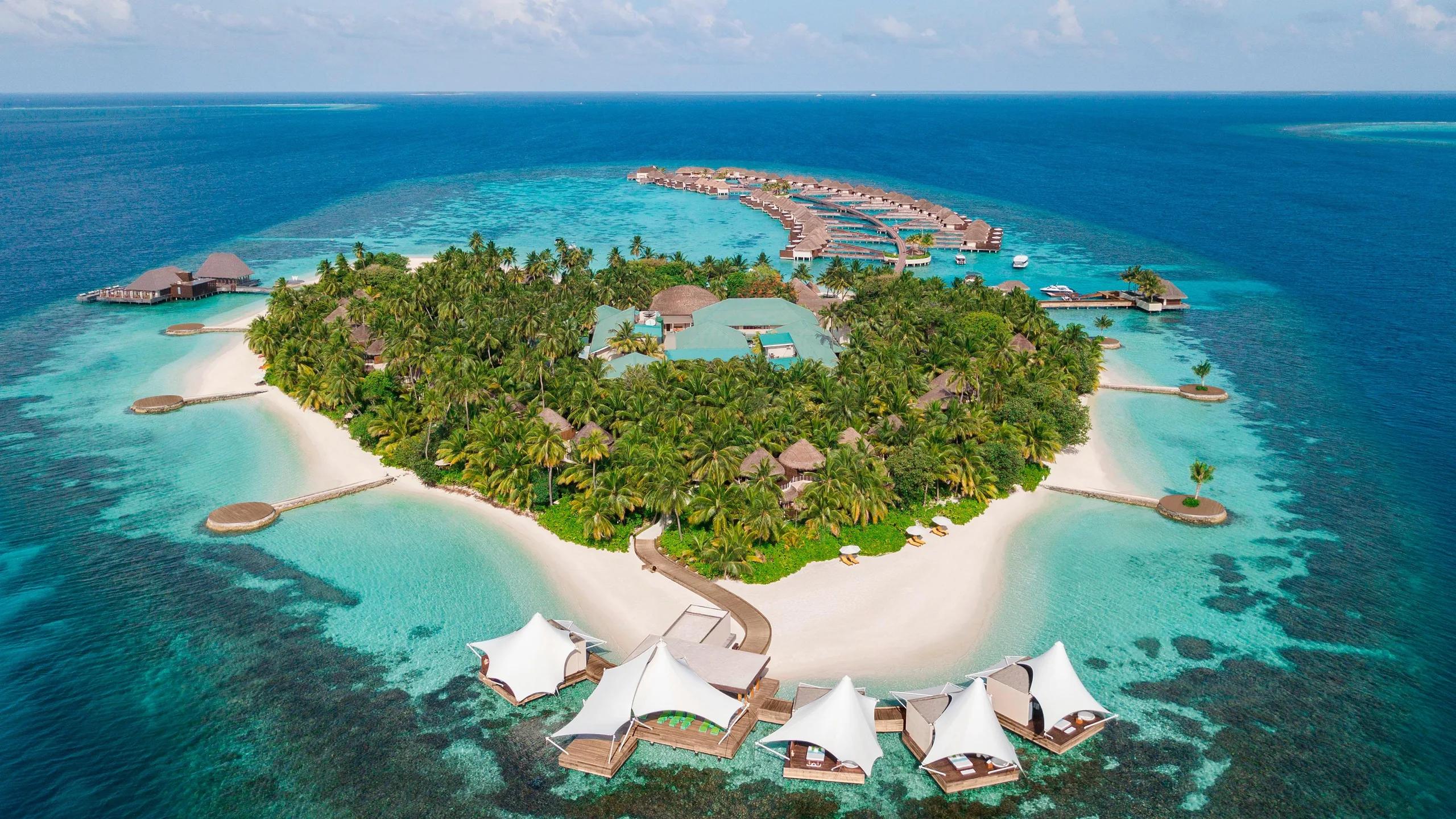 Aerial view of W Maldives' heart-shaped island in North Ari Atoll, with overwater villas reaching into the lagoon and white sail-shaped AWAY Spa pavilions over the water at the point of the island