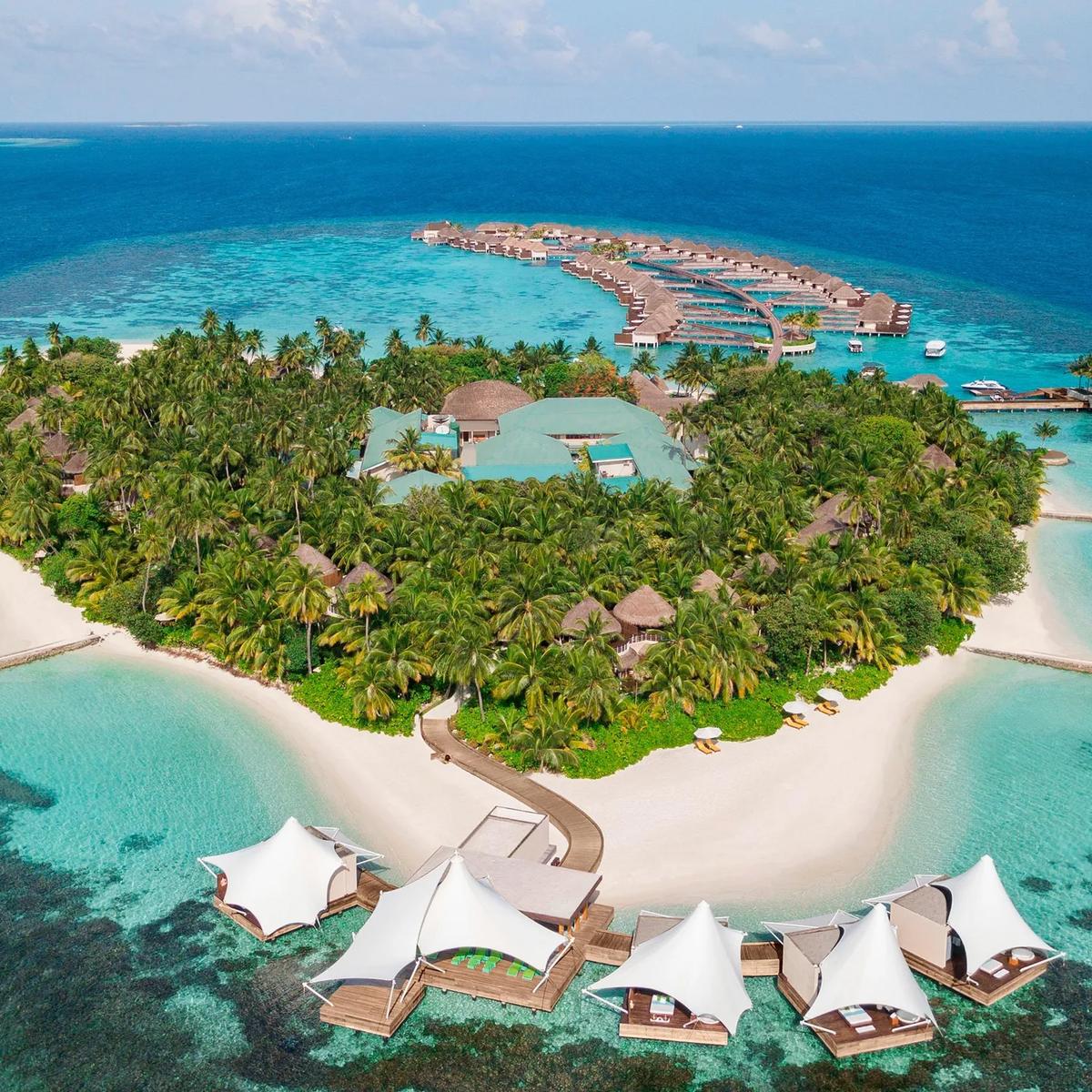 Aerial view of W Maldives' heart-shaped island in North Ari Atoll, with overwater villas reaching into the lagoon and white sail-shaped AWAY Spa pavilions over the water at the point of the island