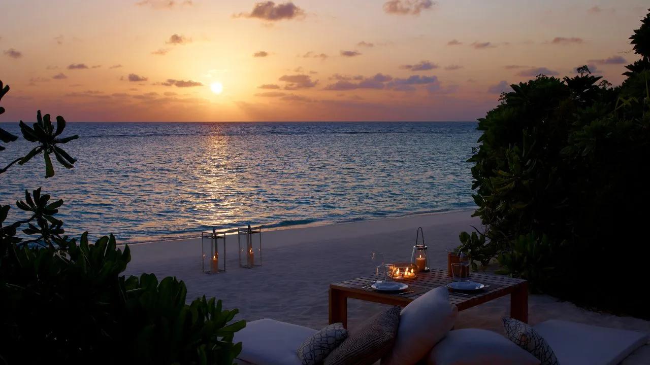 A private beachfront dining table set for two at sunset, part of Dusit Thani Maldives' Borderless Dining concept