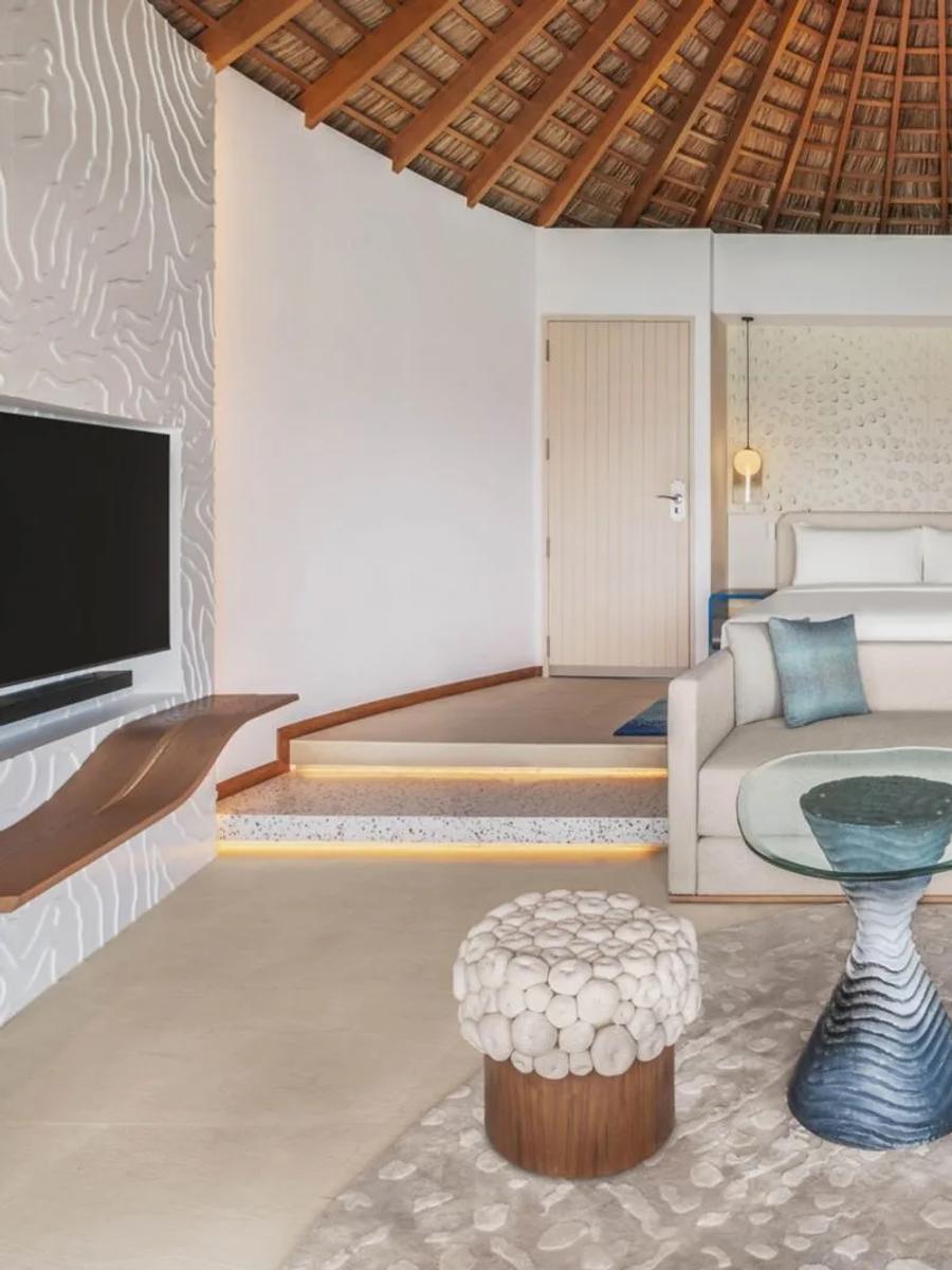 The bedroom of a Superior Overwater villa at W Maldives, under a round thatched roof with a blue-and-orange colour palette