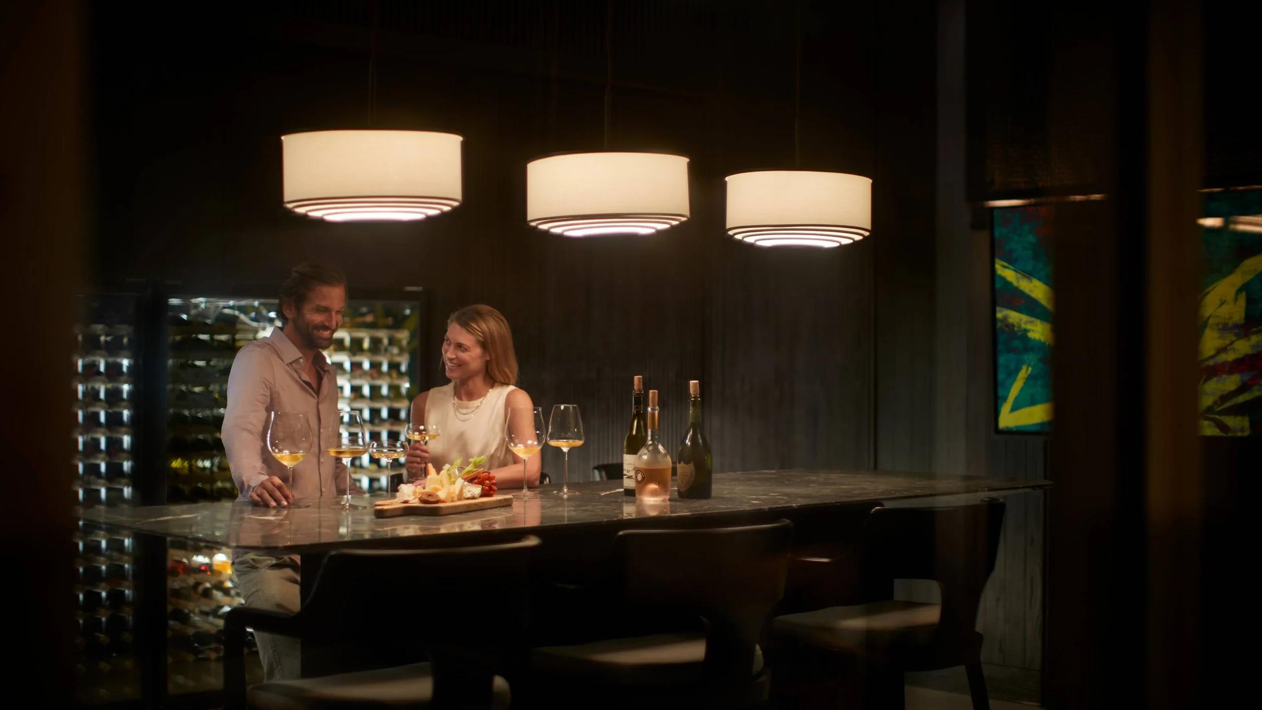 A couple sampling wine and a cheese board at a marble bar beside a glass-walled wine cellar