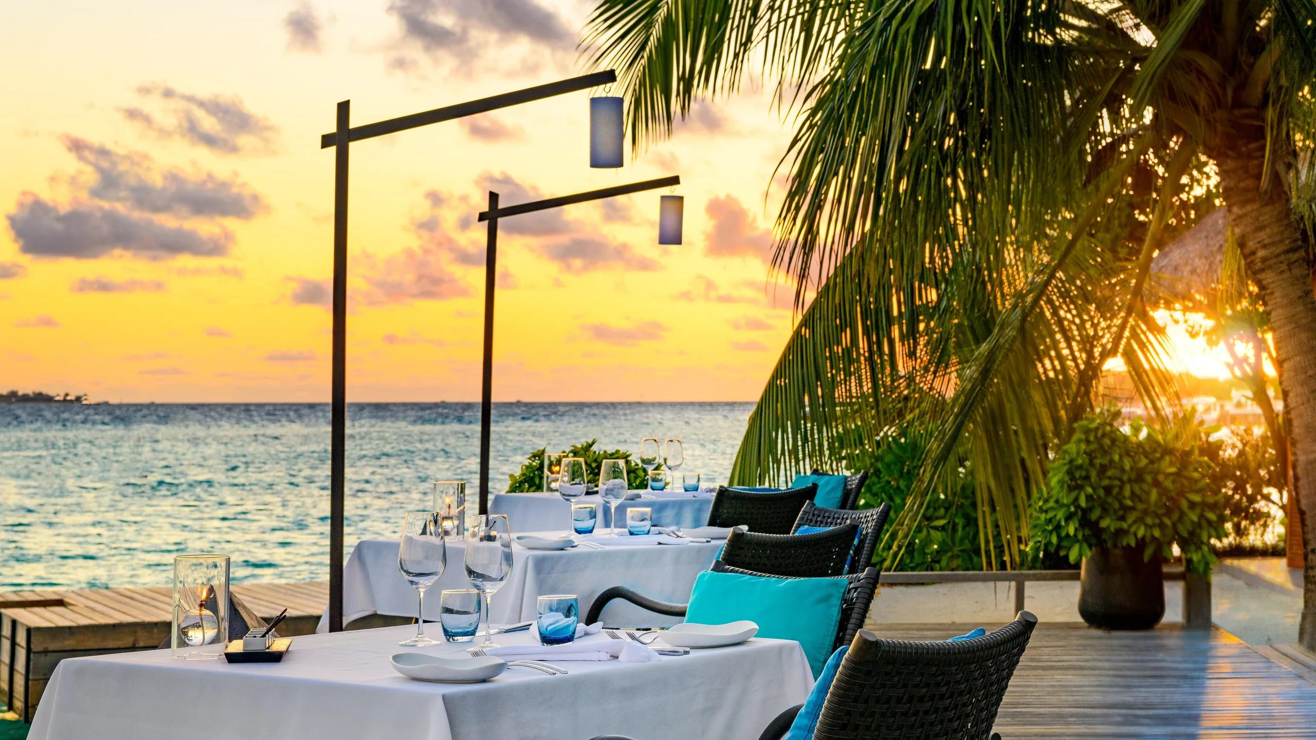 Sea Salt's candlelit beachfront tables set for dinner as the sun sets over the ocean