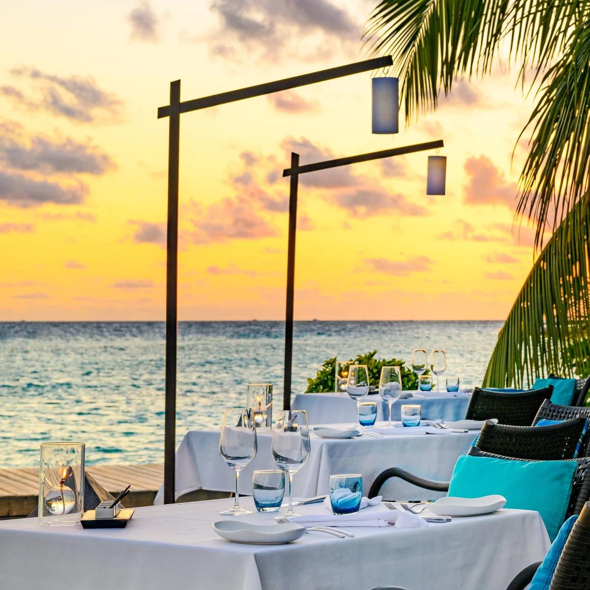 Sea Salt's candlelit beachfront tables set for dinner as the sun sets over the ocean